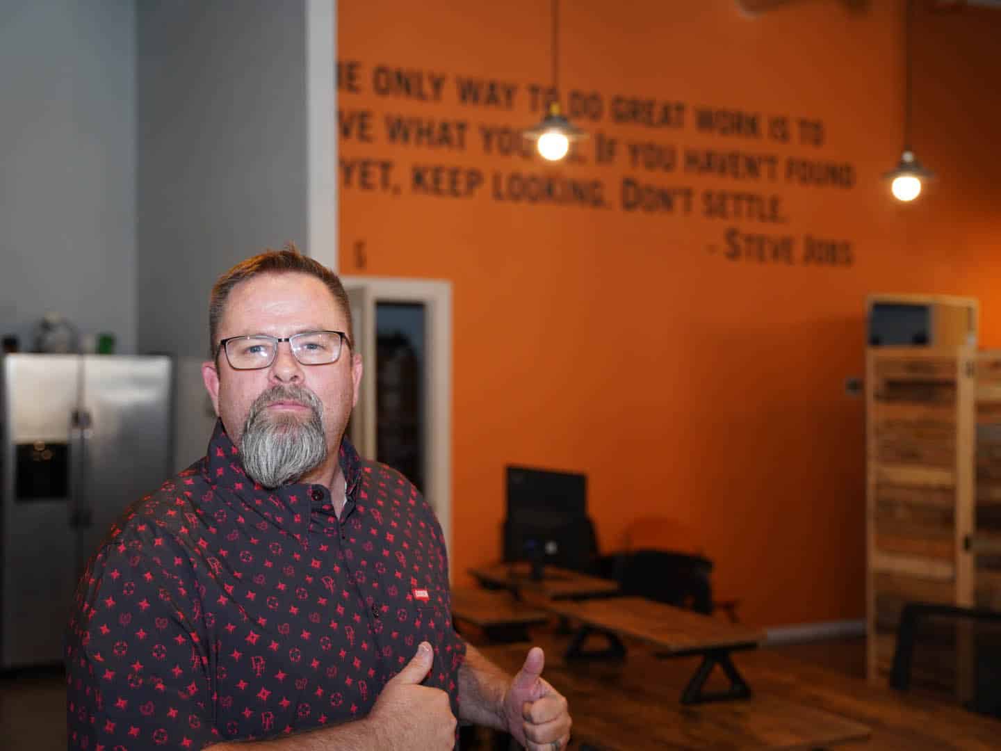Mike Rux giving a thumbs up inside Ciphers Digital Marketing office in Gilbert, AZ, inspired by a Steve Jobs quote on the wall behind him.